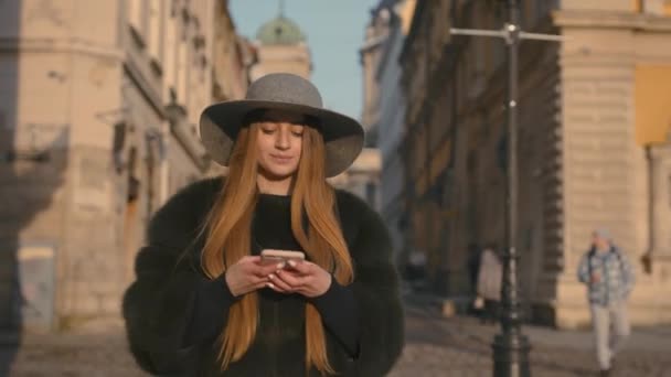 Молода жінка в сірому капелюсі і довге волосся спілкується через смартфон — стокове відео