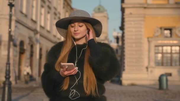 Mujer joven en un sombrero gris y pelo largo se comunica a través de teléfono inteligente — Vídeos de Stock