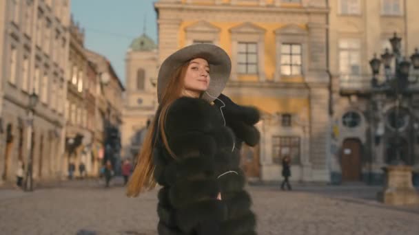 Mladá žena s krásnýma modrýma očima v šedý klobouk pěší ulici se sluchátky — Stock video