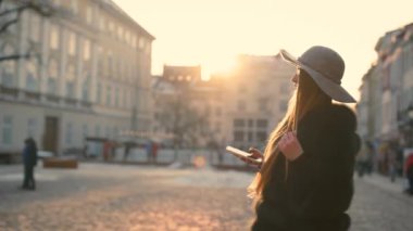 Bir gri şapka ve uzun saçlı güzel mavi gözlü genç kadın gider şehirde smartphone iletişim kurar