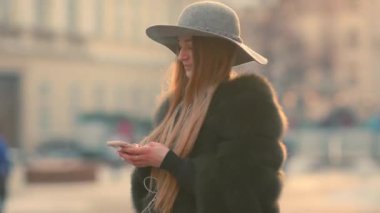 Parlak güneş ışığı altında kadın telefonunu dururken şehir merkezinde kullanır.