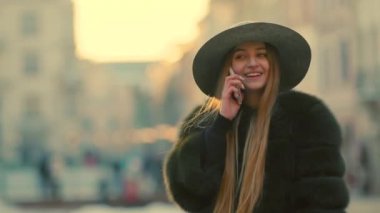 Parlak güneş ışığı altında genç kadın onun telefon gülümseme görüşmeler telefon kullanır.