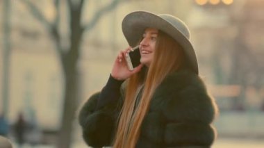 Parlak güneş ışığı altında genç kadın onun telefon gülümseme görüşmeler telefon kullanır.