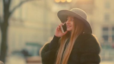 Parlak güneş ışığı altında genç kadın onun telefon gülümseme görüşmeler telefon kullanır.