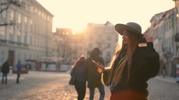 Giovane donna in una luce solare brillante utilizza il suo telefono mentre nel centro della città — Video Stock