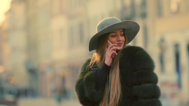 Jovem mulher em uma luz solar brilhante usa seu sorriso telefone fala no telefone — Vídeo de Stock