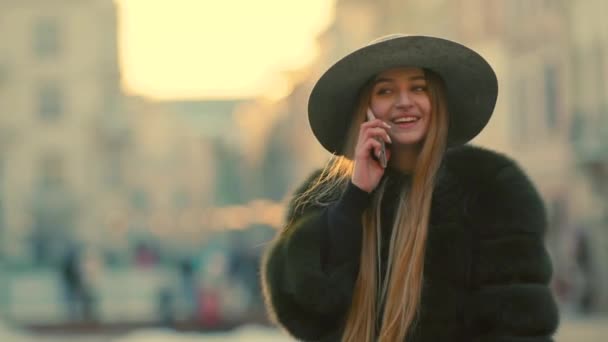 Parlak güneş ışığı altında genç kadın onun telefon gülümseme görüşmeler telefon kullanır. — Stok video