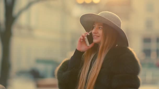 Mujer joven en una luz del sol brillante utiliza su teléfono sonríe habla en el teléfono — Vídeos de Stock