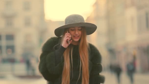 Mujer joven en una luz del sol brillante utiliza su teléfono sonríe habla en el teléfono — Vídeo de stock