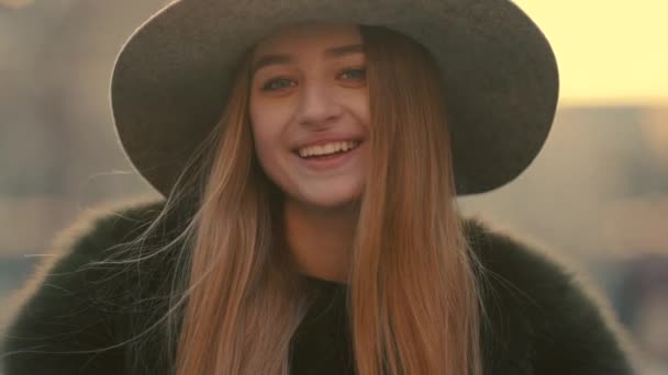 Mujer joven glamurosa en un sombrero gris con encanto mira a la derecha y sonríe hacia la cámara — Vídeos de Stock