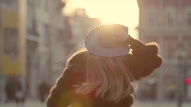 Young woman with long hair, big blue eyes in a gray is rushing in the city-center, than turns to camera and smiles — Stockvideo