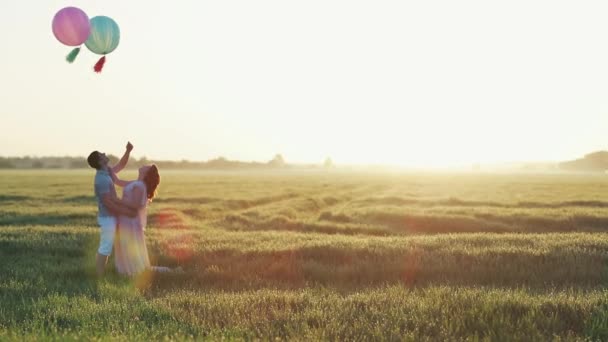 Пара в поле с гелиевыми шарами, обнимающимися и целующимися — стоковое видео