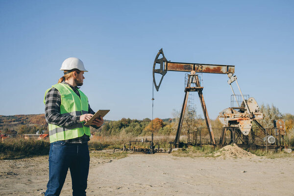 Energy Industry Business Man Holding Device Using Digital Tablet Oil Pump Field. Pumpjack Technician Man Working Digital Tablet Checking Report Oil Pump Farm Job.