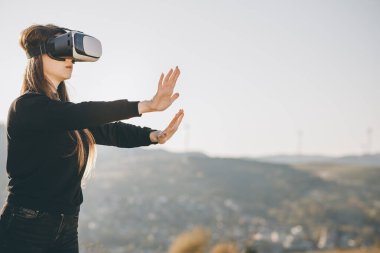 Sanal gerçeklik kulaklığı kullanan tatlı bir kız. Sanal gerçeklik oyunu. VR kulaklık takan bir kadın. Kadın modern VR gözlükleri kullanarak bir şeye dokunuyor.