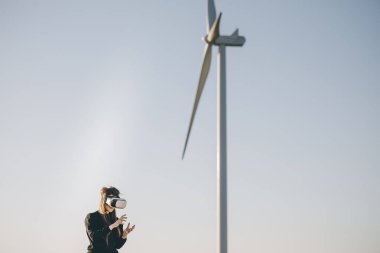 VR kulaklıklı sanal gerçeklik kulaklık kullanan bir mühendis. Mühendis sanal gerçeklik kulaklıklarını taktı ve arka planda rüzgar türbini ile etrafa bakındı..