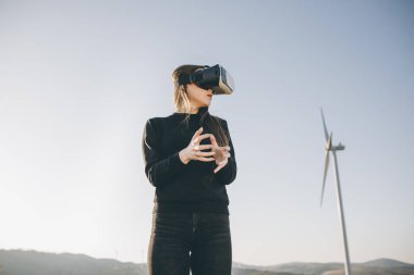 VR gözlüklü mühendis rüzgâr çiftliği. Sanal gerçeklik kulaklığı kullanan bir mühendis. Mühendis sanal gerçeklik kulaklıklarını taktı ve arka planda rüzgar türbini ile etrafa bakındı..