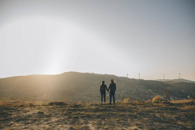 Gün batımında el ele tutuşan romantik bir çift. Aşk ve mutluluk kavramı. El ele tutuşup güneş ışığını yakalım.