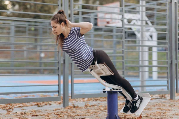 Sporcu kadın üst eklenti bankında yatarken gövdesini kaldırıyor. Atletik adam hiperuzatma yapıyor. Simülatördeki tişörtlü bir kadın parkta aşırı genişleme yapıyor. Fitness. Sağlıklı yaşam tarzı. — Stok fotoğraf