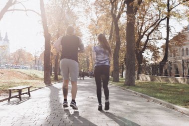 Genç adam ve kız spor yapıyor. Güneşli parkta koşan spor çifti. Spor eğitiminde erkek ve kadın birlikte. Atletik yeni evliler birlikte egzersiz yapıyorlar. Spor çifti parkta birlikte koşar..