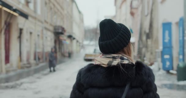 Atrakcyjna dziewczyna w czarnym płaszczu z czerwonymi ustami idzie ulicą w mieście, niż zwraca się do kamery i uśmiecha. — Wideo stockowe