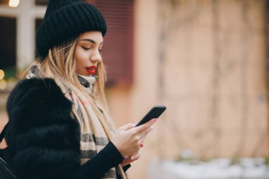 Şehir merkezinde soğuk havada cep telefonu kullanan bir kadın. Teknoloji, kış ve tatil konsepti. Kış Tatili 'nden Hoşlanan Kız, Sosyal ağ, uygulama kullanarak