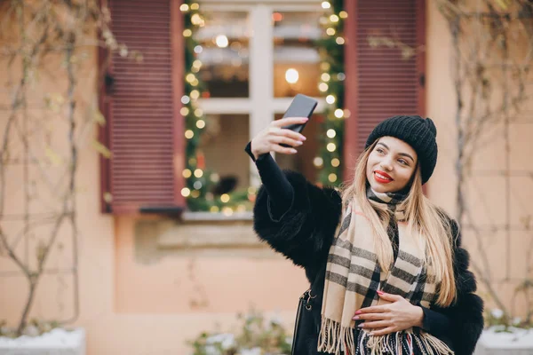 Akıllı telefondan selfie çekiyoruz. Güzel bir kızın portresi. Sokakta akıllı telefondan selfie çekiyor. Lüks kıyafetler içinde dışarıda fotoğraf çeken seksi bir kadın. Şehir sokağının yakınında kendi portresini çeken bir kadın. — Stok fotoğraf