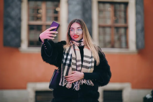 Akıllı telefondan selfie çekiyoruz. Güzel bir kızın portresi. Sokakta akıllı telefondan selfie çekiyor. Lüks kıyafetler içinde dışarıda fotoğraf çeken seksi bir kadın. Şehir sokağının yakınında kendi portresini çeken bir kadın. — Stok fotoğraf