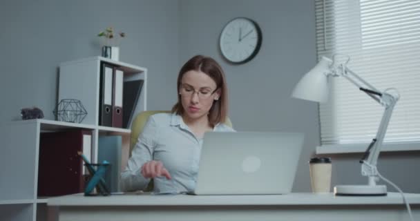 Mujer atractiva en gafas de vista disfrutando de su trabajo freelance favorito trabajando en casa en computadora portátil. Freelancer femenina usando smartphone, netbook y escribiendo ideas en bloc de notas — Vídeos de Stock