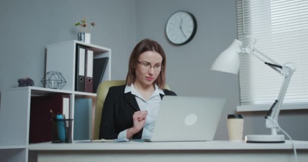 若い美しいブルネットはロフトオフィスのクールなクリエイティブエージェンシーのラップトップコンピュータで動作します。彼女はテイクアウェイコーヒーと彼女のテーブルのノートを持っています — ストック動画