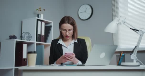 Empresaria confiada que trabaja en una computadora portátil en su oficina moderna. Elegante hermosa mujer haciendo trabajo importante. Mujer joven hermosa y creativa sentada en su escritorio usando computadora portátil . — Vídeos de Stock