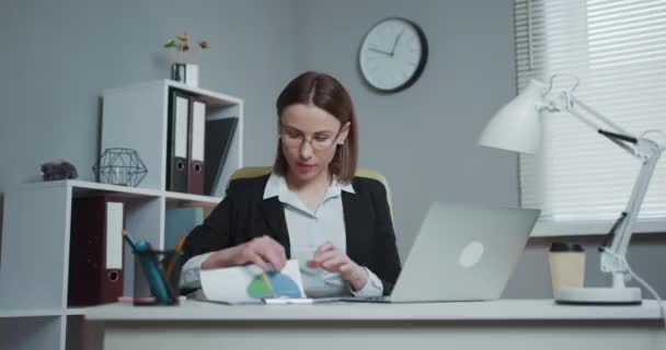 職場における女性専用オフィスワーカーのポート。現代オフィスの職場で財務書類からのデータを扱う若いビジネスマンを自信を持って. — ストック動画