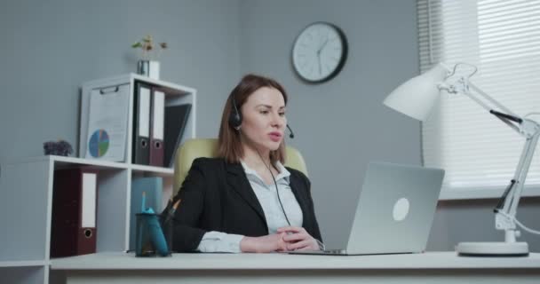 Woman in Headphones Holding Paper Financial Report talk at Webcam make video call in office, business coach looking at camera speak show statistics explain marketing strategy for client — 비디오