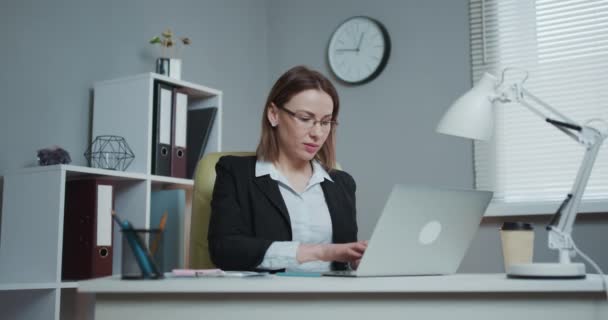 Retrato de mujer de negocios con gafas sonrisa mientras está sentado en la mesa con el ordenador portátil, mira a la cámara. Concepto gente de negocios — Vídeos de Stock