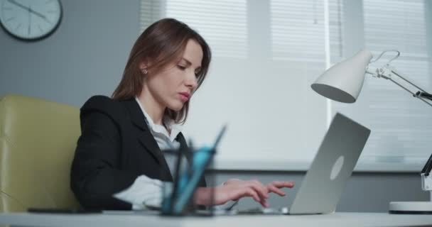 La mujer está usando el ordenador portátil mientras está sentada en su escritorio. La joven empresaria está sentada en la oficina y trabajando en el cuaderno — Vídeos de Stock