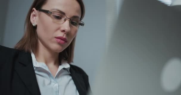 De vrouw gebruikt een laptop terwijl ze aan haar bureau zit. Jonge Europese zakenvrouw zit in het kantoor en werkt aan notebook — Stockvideo