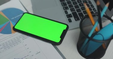 Ofis masasında yeşil ekran, dijital tablet ve grafik iş diyagramı olan akıllı telefonlu iş belgeleri