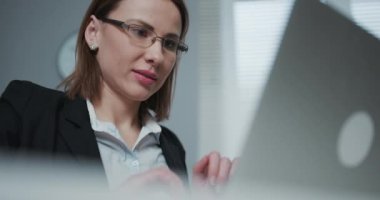 Kadın masasında otururken dizüstü bilgisayar kullanıyor. Avrupalı genç iş kadını ofiste oturuyor ve defter üzerinde çalışıyor.