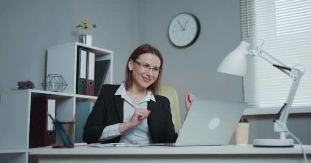 A jovem criativa dança enquanto se senta em sua mesa de trabalho. Retrato da bela empresária dançando enquanto se senta em sua mesa. Mulher bem sucedida e feliz comemorando vendas recordes . — Vídeo de Stock