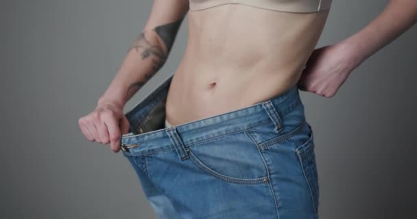 Jeune femme montre sa perte de poids et de porter son vieux jeans. Fille mince en gros jeans montrant comment elle perdait du poids quand elle a commencé à manger des aliments sains — Video