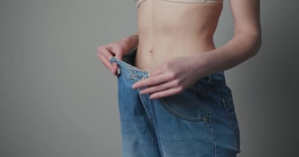 Γυναίκα δείχνει την απώλεια βάρους της και φοράει παλιά τζιν της. Λεπτό κορίτσι σε μεγάλα τζιν δείχνει πώς έχανε βάρος όταν άρχισε να τρώει υγιεινά τρόφιμα. — Αρχείο Βίντεο