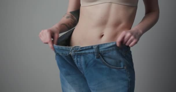 Viktminskning och kroppsuppfattning. Unga kvinna visar sin viktminskning och bär sina gamla jeans. Slim flicka i stora jeans visar hur hon gick ner i vikt när hon började äta hälsosam mat. — Stockvideo