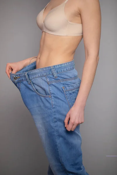 Donna mostra la sua perdita di peso e indossa i suoi vecchi jeans. Slim ragazza in grandi jeans che mostra come stava perdendo peso quando ha iniziato a mangiare cibo sano . — Foto Stock