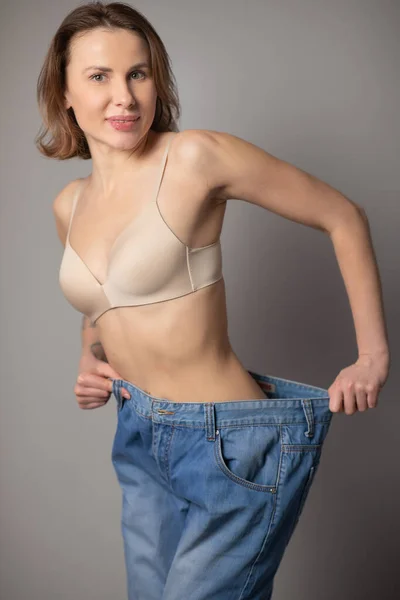 Frau nach Diät abnehmen, abnehmen, Fett verbrennen und flache Taille. Dünne Mädchen zeigen Gewichtsverlust und alte dicke Jeans. Magerer weiblicher Bauch trägt zu große Hosen. — Stockfoto