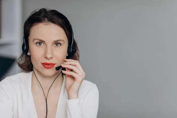 Attractive young female customer service agent talking to a customer with a telephony headset as she looks at the camera
