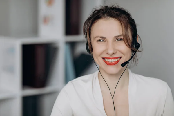 Pretty woman talking with headset in a call center looking camera. Attractive young female customer service agent talking to a customer with a telephony headset as she looks at the camera