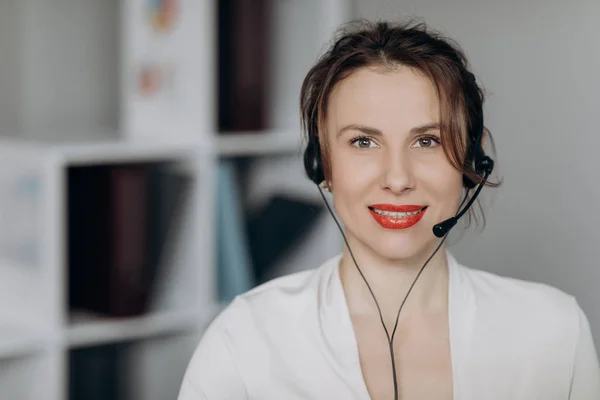 Young female customer service agent talking to a customer with a telephony headset as she looks at the camera.