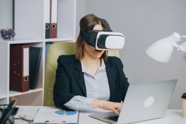 Ofiste sanal gerçeklik gözlüğü takan bir kadın. VR gözlük takan genç bir kız. İş yerinde artırılmış gerçeklikte çalışan güzel bir kadın..