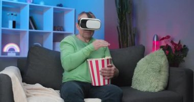 Son sınıf öğrencisi elinde patlamış mısırla sanal gerçeklik gözlüğü takıyor ve VR ekranı ile elini kaldırıyor.