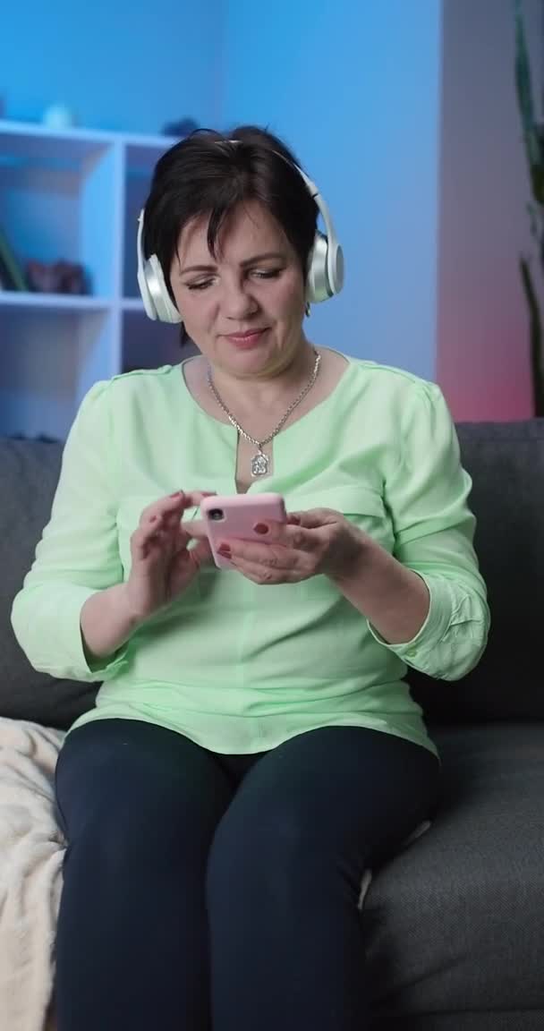 Alegre Divertido Silly Senior Mujer escuchando música con auriculares inalámbricos grandes. Positive Pensioner Meloman Singing to Music (en inglés). Vida moderna activa después de la jubilación — Vídeo de stock