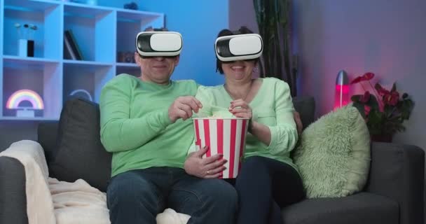 Eccitato maturo anziano coppia è divertirsi utilizzando VR occhiali in salotto guardando il film a casa. Coppia anziana che utilizza la tecnologia moderna. Coppia di famiglie è seduto sul divano e guardare la TV — Video Stock